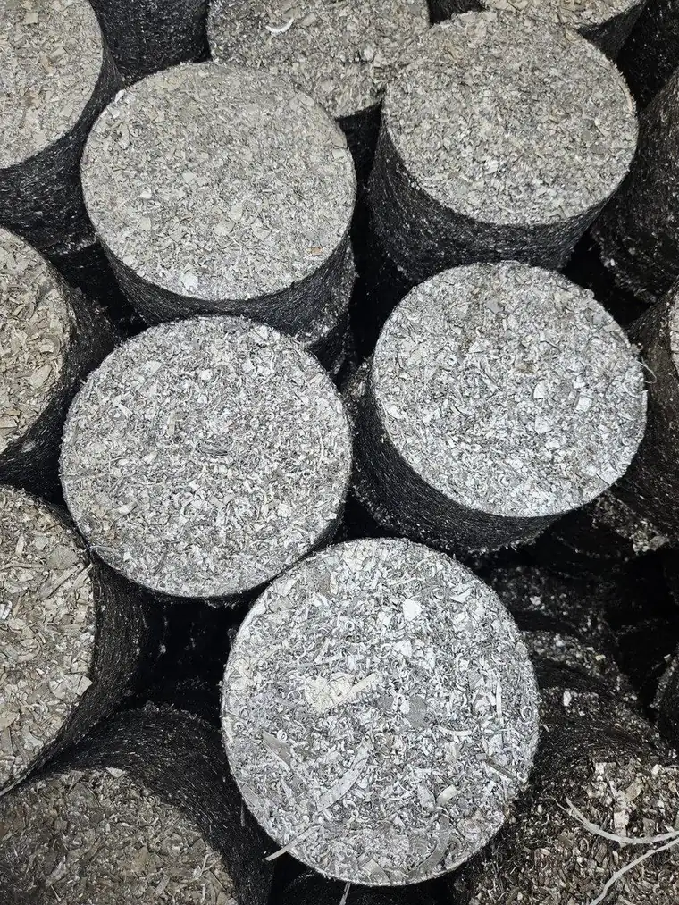 Close-up of stacked cylindrical metal briquettes, bright compressed stainless turnings visible across the pressed faces.