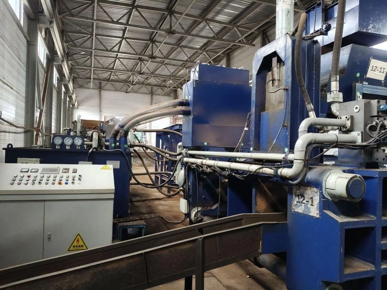 Wide view of the briquetting press line: hydraulic power unit with three pressure gauges, a control cabinet, and blue press housings.