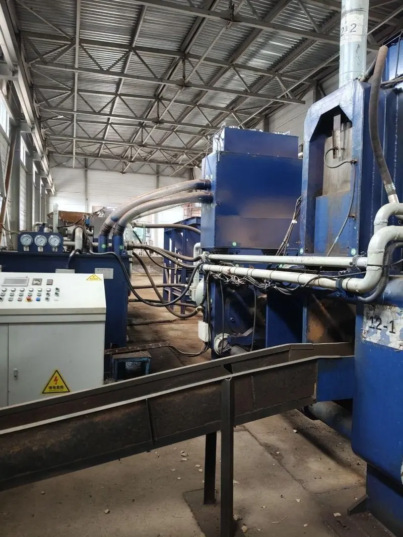 Blue hydraulic briquetting press marked 12-1 with hydraulic hoses and a control panel alongside it.